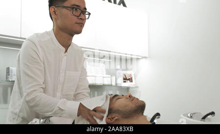 Die Asiatischer mann Friseur wäscht den Kopf des Client und wischt es mit einem Handtuch Stockfoto