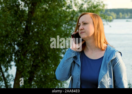 Frau mittleren Alters, am Telefon zu sprechen. Hintergrund des Flusses Stockfoto