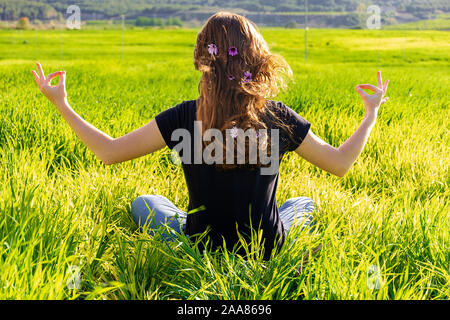 Junge kaukasier Frau rot - mit Sommersprossen blonde, ruht auf der grünen Wiese am Frühling Sonnenuntergang, sitzen in einem Yoga Position. Meditation, Achtsamkeit, entspannen Stockfoto