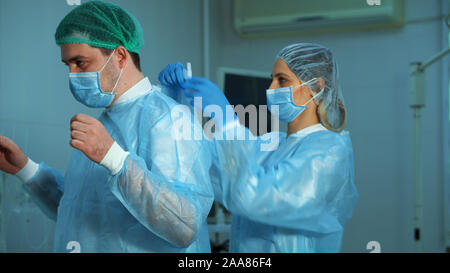 Der Arzt ist Vorbereitung für die Chirurgie. Krankenschwester hilft dem Arzt einen Bademantel im Operationssaal zu tragen Stockfoto