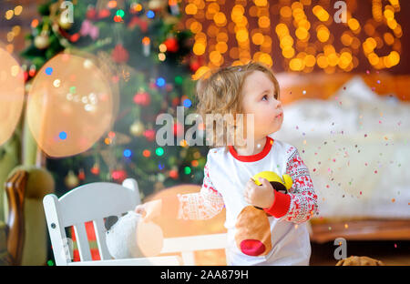 Cute Baby in Pyjamas spielt in einem festlich dekorierten Zimmer, vor dem Hintergrund der hellen Lichter Stockfoto