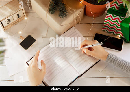 Schreibt wünsche. Träume der Ziele plant, machen Sie eine Liste für das Schreiben im Notebook. Weibliche Hände auf einem Hintergrund mit Holz- Kalender, Geschenkset für das Neue Jahr, winter Urlaub und Weihnachten. Vorbereitung Moodboard. Stockfoto