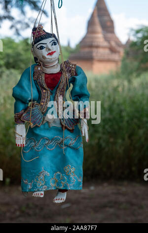 Traditionelle Burmesische hölzerne Marionette in einem aufwendigen Kostüm hängt von einem Baum mit einem antiken Tempel von Bagan, Myanmar im Hintergrund Stockfoto