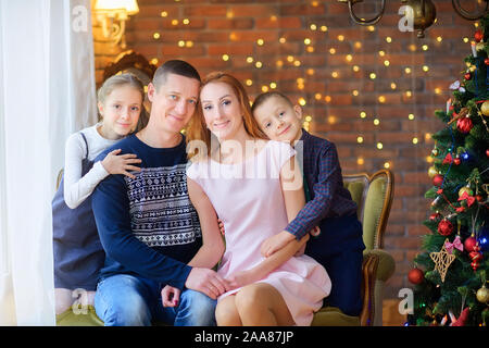 Porträt einer glücklichen Familie sitzt auf einem Sofa in der Nähe des festlichen Weihnachtsbaum. Warten auf den Urlaub Stockfoto