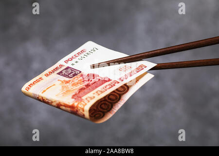 Chinese sticks halten Aufgerollt fünf Tausend Rubel, close-up. Das Konzept der Beziehungen zwischen Russland und China Stockfoto