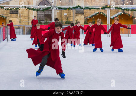 Winchester, Hampshire, UK. 20. November 2019. Chorknaben Schlittschuhlaufen auf der Eisbahn in ihrer berühmten roten Roben an der Winchester Cathedral als Weihnachtsfeier erhalten unterwegs mit der festliche Tradition der Vorsänger Skaten rund um die Eisbahn vor seiner Eröffnung morgen. Die Eisbahn ist Teil der Kathedrale von Winchester Weihnachtsmarkt, einer der grössten im Land. Credit: Carolyn Jenkins/Alamy leben Nachrichten Stockfoto