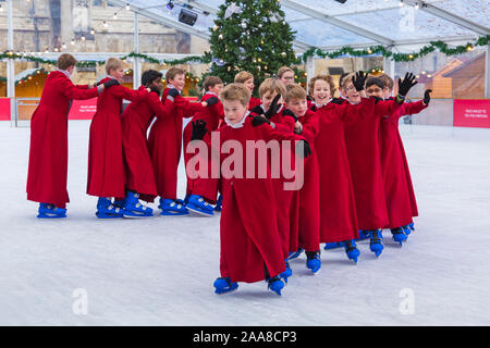 Winchester, Hampshire, UK. 20. November 2019. Chorknaben Schlittschuhlaufen auf der Eisbahn in ihrer berühmten roten Roben an der Winchester Cathedral als Weihnachtsfeier erhalten unterwegs mit der festliche Tradition der Vorsänger Skaten rund um die Eisbahn vor seiner Eröffnung morgen. Die Eisbahn ist Teil der Kathedrale von Winchester Weihnachtsmarkt, einer der grössten im Land. Credit: Carolyn Jenkins/Alamy leben Nachrichten Stockfoto