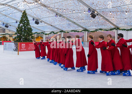 Winchester, Hampshire, UK. 20. November 2019. Chorknaben Schlittschuhlaufen auf der Eisbahn in ihrer berühmten roten Roben an der Winchester Cathedral als Weihnachtsfeier erhalten unterwegs mit der festliche Tradition der Vorsänger Skaten rund um die Eisbahn vor seiner Eröffnung morgen. Die Eisbahn ist Teil der Kathedrale von Winchester Weihnachtsmarkt, einer der grössten im Land. Credit: Carolyn Jenkins/Alamy leben Nachrichten Stockfoto