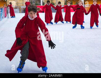 Winchester, Hampshire, UK. 20. November 2019. Chorknaben Schlittschuhlaufen auf der Eisbahn in ihrer berühmten roten Roben an der Winchester Cathedral als Weihnachtsfeier erhalten unterwegs mit der festliche Tradition der Vorsänger Skaten rund um die Eisbahn vor seiner Eröffnung morgen. Die Eisbahn ist Teil der Kathedrale von Winchester Weihnachtsmarkt, einer der grössten im Land. Credit: Carolyn Jenkins/Alamy leben Nachrichten Stockfoto