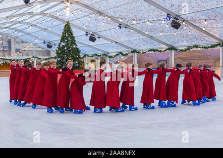 Winchester, Hampshire, UK. 20. November 2019. Chorknaben Schlittschuhlaufen auf der Eisbahn in ihrer berühmten roten Roben an der Winchester Cathedral als Weihnachtsfeier erhalten unterwegs mit der festliche Tradition der Vorsänger Skaten rund um die Eisbahn vor seiner Eröffnung morgen. Die Eisbahn ist Teil der Kathedrale von Winchester Weihnachtsmarkt, einer der grössten im Land. Credit: Carolyn Jenkins/Alamy leben Nachrichten Stockfoto