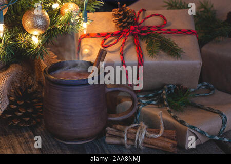 Nahaufnahme der heiße Schokolade in eine braune Tasse mit Weihnachten Geschenke und Baum im Hintergrund auf einem rustikalen hölzernen Oberfläche Stockfoto