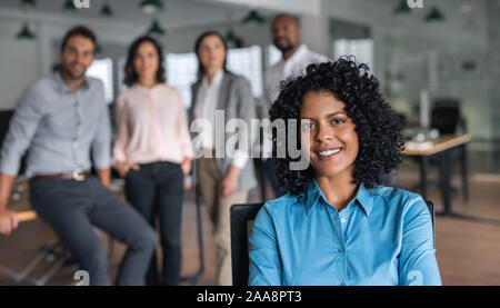 Lächelnd Geschäftsfrau in einem Büro mit Kollegen hinter ihr sitzen Stockfoto