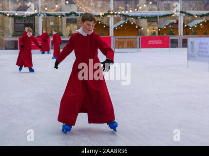 Winchester, Hampshire, UK. 20. November 2019. Chorknaben Schlittschuhlaufen auf der Eisbahn in ihrer berühmten roten Roben an der Winchester Cathedral als Weihnachtsfeier erhalten unterwegs mit der festliche Tradition der Vorsänger Skaten rund um die Eisbahn vor seiner Eröffnung morgen. Die Eisbahn ist Teil der Kathedrale von Winchester Weihnachtsmarkt, einer der grössten im Land. Credit: Carolyn Jenkins/Alamy leben Nachrichten Stockfoto