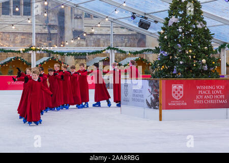 Winchester, Hampshire, UK. 20. November 2019. Chorknaben Schlittschuhlaufen auf der Eisbahn in ihrer berühmten roten Roben an der Winchester Cathedral als Weihnachtsfeier erhalten unterwegs mit der festliche Tradition der Vorsänger Skaten rund um die Eisbahn vor seiner Eröffnung morgen. Die Eisbahn ist Teil der Kathedrale von Winchester Weihnachtsmarkt, einer der grössten im Land. Credit: Carolyn Jenkins/Alamy leben Nachrichten Stockfoto