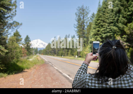 Frau am Straßenrand unter Bild von Mount Shasta auf Ihrem Telefon Stockfoto