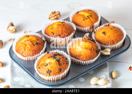 Vanille Karamell Muffins in Pappbechern in backgeräte auf weißem Holz- Hintergrund. Köstliche Kuchen mit Rosinen, Mandeln und Nüsse. Hausgemachte Kekse Kuchen Stockfoto