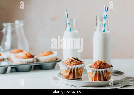 Vanille Karamell Muffins in Pappbechern und botlles von Milch auf weißem Holz- Hintergrund. Köstliche Kuchen mit Rosinen, Mandeln und Nüsse. Hausgemachte biscu Stockfoto