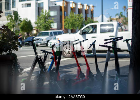 Elektroroller aufgereiht auf dem Bürgersteig einer belebten Straße Stockfoto