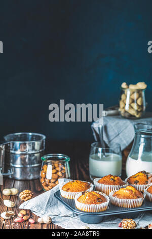 Vanille Karamell Muffins in Pappbechern und Glas in backgeräte von Milch auf dunklem Hintergrund. Köstliche Kuchen mit Rosinen, Mandeln und Nüsse. Home Stockfoto