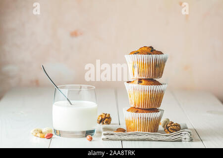 Vanille Karamell Muffins in Pappbechern und Glas Milch auf weißem Holz- Hintergrund. Köstliche Kuchen mit Rosinen, Mandeln und Nüsse. Hausgemachte Kekse Stockfoto