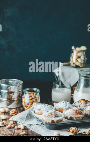 Vanille Karamell Muffins in Pappbechern und Glas in backgeräte von Milch auf dunklem Hintergrund. Köstliche Kuchen mit Rosinen, Mandeln und Nüsse. Home Stockfoto