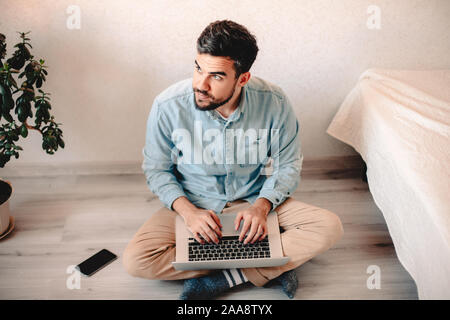 Mann mit Laptop Computer, während auf dem Boden zu Hause sitzen Stockfoto