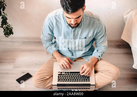 Junger Mann mit Laptop Computer, während auf dem Boden zu Hause sitzen Stockfoto