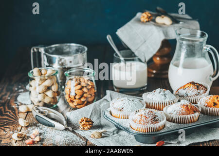 Vanille Karamell Muffins in Pappbechern und Glas in backgeräte von Milch auf dunklem Hintergrund. Köstliche Kuchen mit Rosinen, Mandeln und Nüsse. Home Stockfoto