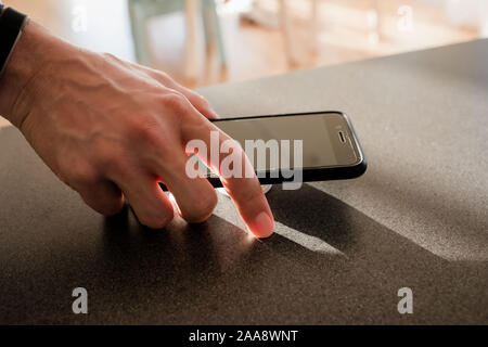 Mans hand mit einem Telefon in der Küche zu Hause. Stockfoto