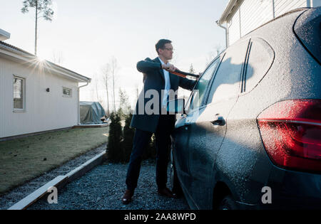 Business mann Eis kratzen von seinem Auto am Morgen vor der Arbeit Stockfoto