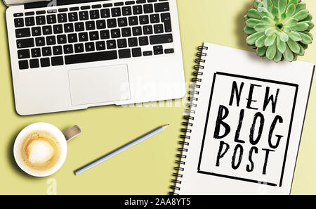 Blick von oben auf die Worte neuen Blog-eintrag auf spiral Notizblock Geschrieben am Schreibtisch mit Laptop und Topfpflanze Stockfoto
