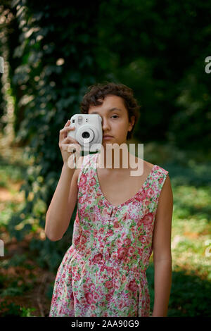 Adorable jugendliche Mädchen, dass sofortige Kamera und Foto schließen Augen im Green Park Stockfoto