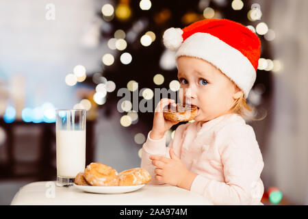 Baby Mädchen essen Cookie mit Milch in der Nähe von Xmas Tree Stockfoto