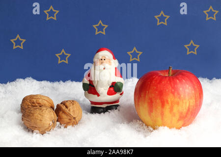 Sankt Nikolaus oder Weihnachtsmann Figur stehend im Schnee zwischen Walnüssen und einem Apple vor einem dunkelblauen Himmel Stockfoto