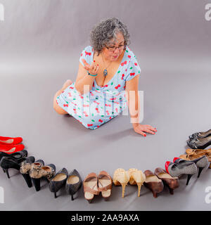 Unentschlossen, reife Frau die Auswahl aus einer Vielzahl von Schuhen, Gruppe von hochhackige Schuhe in verschiedenen fashion styles auf dem Boden Stockfoto
