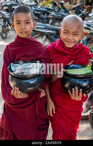 Zwei junge buddhistische Mönche mit opferschalen mit Opfergaben und Geld gefüllt und in leuchtenden roten Roben gekleidet mit unschuldigem Lächeln Stockfoto