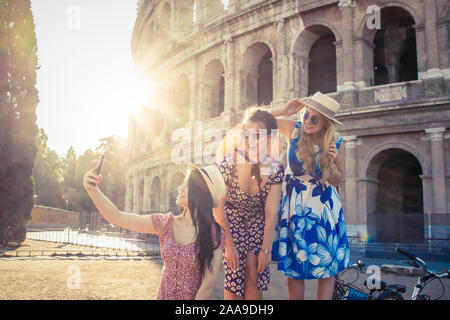 Drei glückliche junge Frauen Freunde Touristen mit Fahrrädern unter selfies am Kolosseum in Rom, Italien bei Sonnenaufgang. Stockfoto