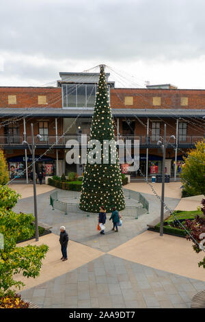 Weihnachtskäufer hinter einem großen Weihnachtsbaum in der Mitte des Gunwharf Quays in Portsmouth, Hampshire, Großbritannien Stockfoto