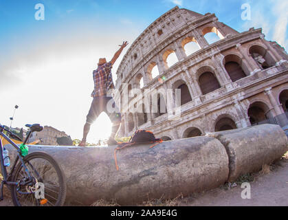 Glückliche junge Mann Touristen mit dem Fahrrad tragen Shirt und Hut auf eine Spalte Aufnehmen von Bildern am Kolosseum in Rom, Italien bei Sonnenaufgang stehen. Stockfoto