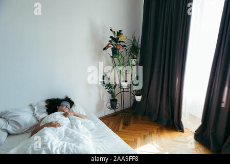 Frau mit schlafbrille im Bett morgen Licht durch Vorhänge Stockfoto