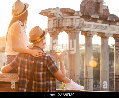 Junges Paar Tourist mit Glas Weißwein am Forum Romanum bei Sonnenaufgang. Historische imperial Foro Romano in Rom, Italien ab Panorama Sicht. Stockfoto