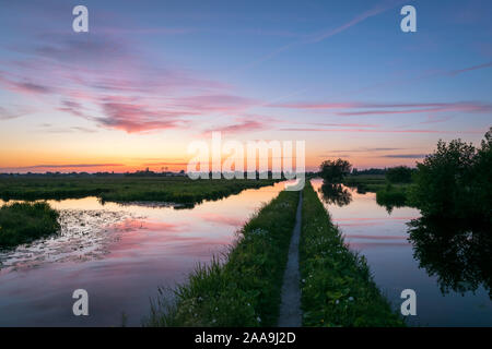 Roter Sonnenuntergang über die niederländische Landschaft in der Nähe der Stadt Gouda, Niederlande. Ein Pfad führt in den Abstand zwischen zwei Kanälen. Stockfoto