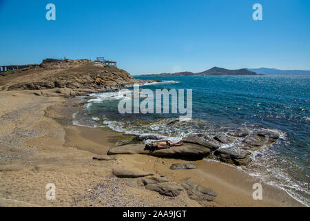 Naxos, Griechenland - 12. Juli 2019: Mann, Sonnenbaden auf den Felsen in der Nähe von Naxos Chora von kristallklarem Meer Stockfoto