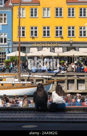 Kopenhagener Uferpromenade, Blick im späten Frühjahr auf zwei junge Frauen, die am Nyhavn Kai sitzen und die Aktivitäten im geschäftigen Hafengebiet von Kopenhagen beobachten. Stockfoto