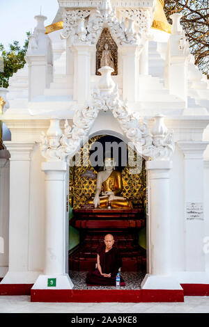 Ein buddhistischer Mönch sitzt vor einer Statue, die Shwedagon Pagode, Yangon, Myanmar. Stockfoto