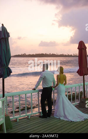 Rückansicht der neu verheirateten umarmen sich und Sonnenuntergang Skyline auf der tropischen Insel Strand auf den Malediven. Türkisfarbene meer Lagune auf Hintergrund Stockfoto