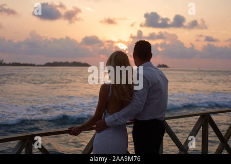 Rückansicht der neu verheirateten umarmen sich und Sonnenuntergang Skyline auf der tropischen Insel Strand auf den Malediven. Türkisfarbene meer Lagune auf Hintergrund Stockfoto