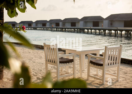 Weiße leere Tabelle Tisch und Stühle im Tropical resrraunt am Strand auf den Malediven. Blue Ocean Lagune und Wasser Bungalows auf Hintergrund. Keine Menschen. Stockfoto