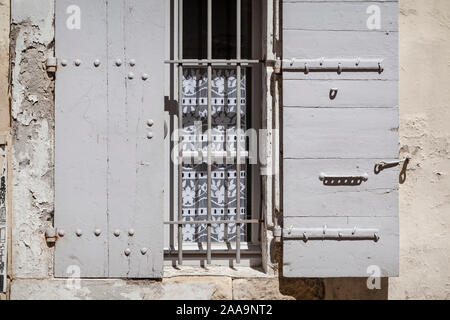 Fenster eines Hauses mit Grau lackiert traditionellen Fensterläden aus Holz und Gardinen auf einer Straße in Arles, Südfrankreich. Stockfoto