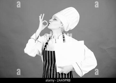 Glückliche Frau Kochen gesund essen von Rezept. Menü im Restaurant. Kulinarische nähren. Frau in Cook hat und Schürze. professioneller Koch in der Küche. Küche. Hausfrau mit Kochbuch. Die Auswahl von Lebensmitteln. Stockfoto